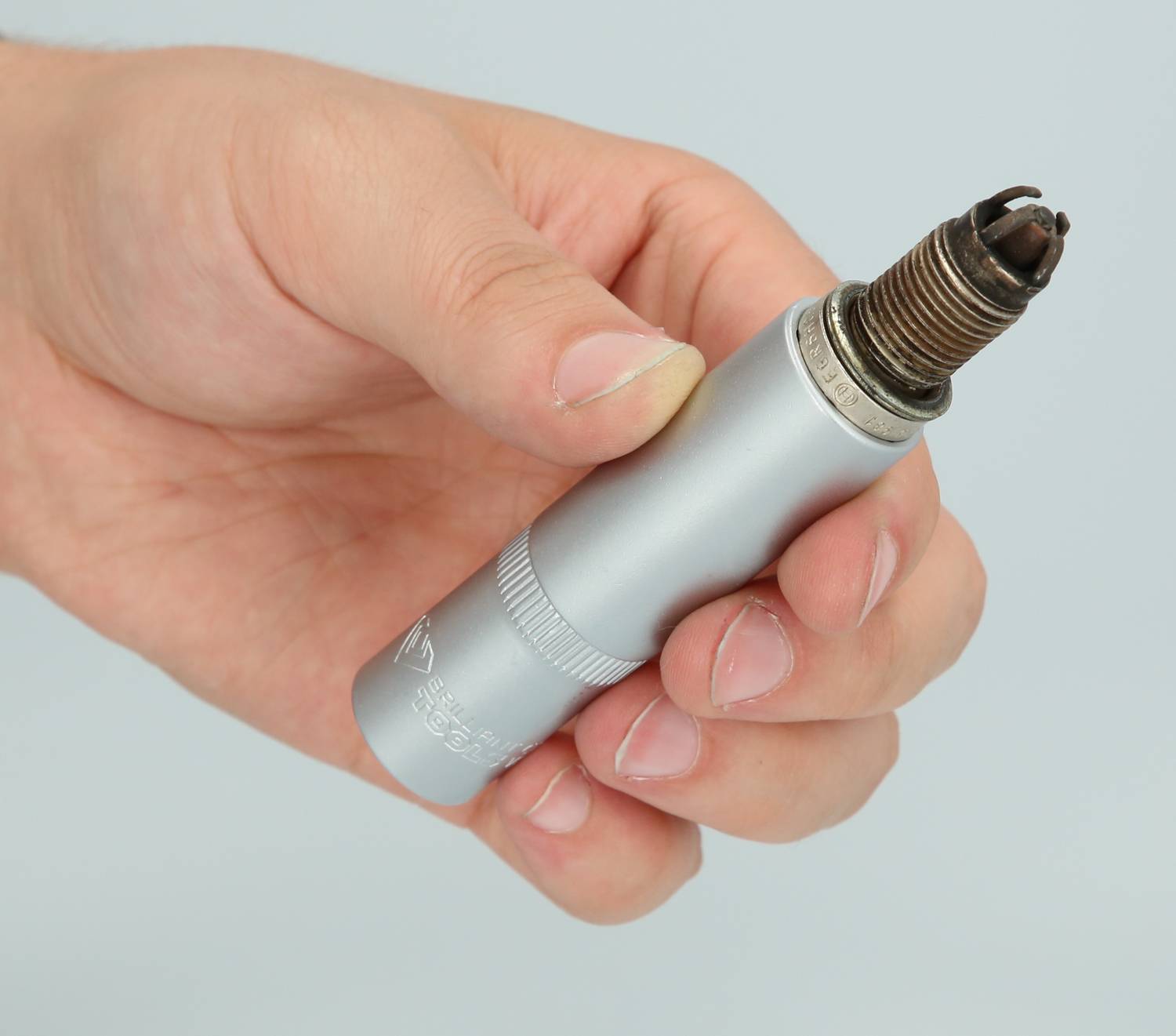 A hand is holding a silver spark plug, an important automotive component used to ignite fuel in the engine.