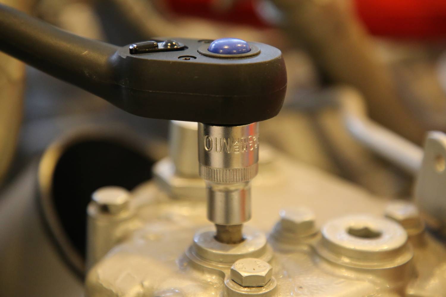 A torque wrench tightens a screw on a metallic device. The lever handle is black with a blue button.