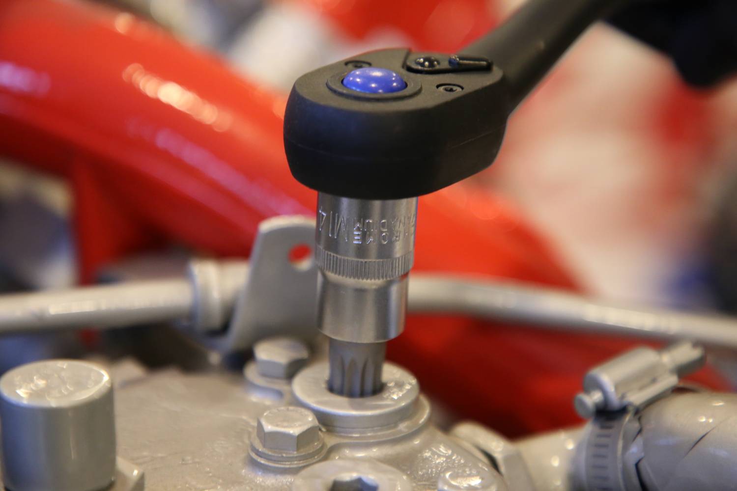 'Close-up of a spanner working on a metal valve, surrounded by a red and silver machine component.'
