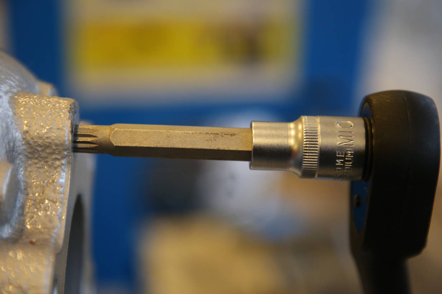 Close-up of a torque wrench positioned on a screw component. Focus on precision measurement in a workshop environment.