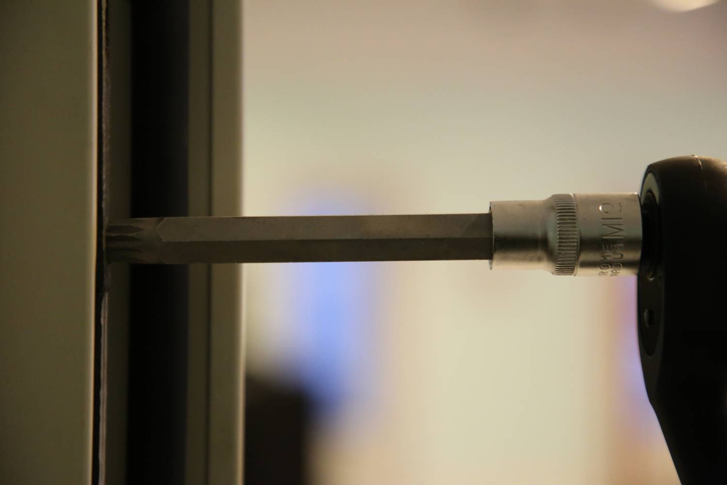 A screwdriver is inserted into a recess on a metal frame. Details of the surrounding area are blurred.