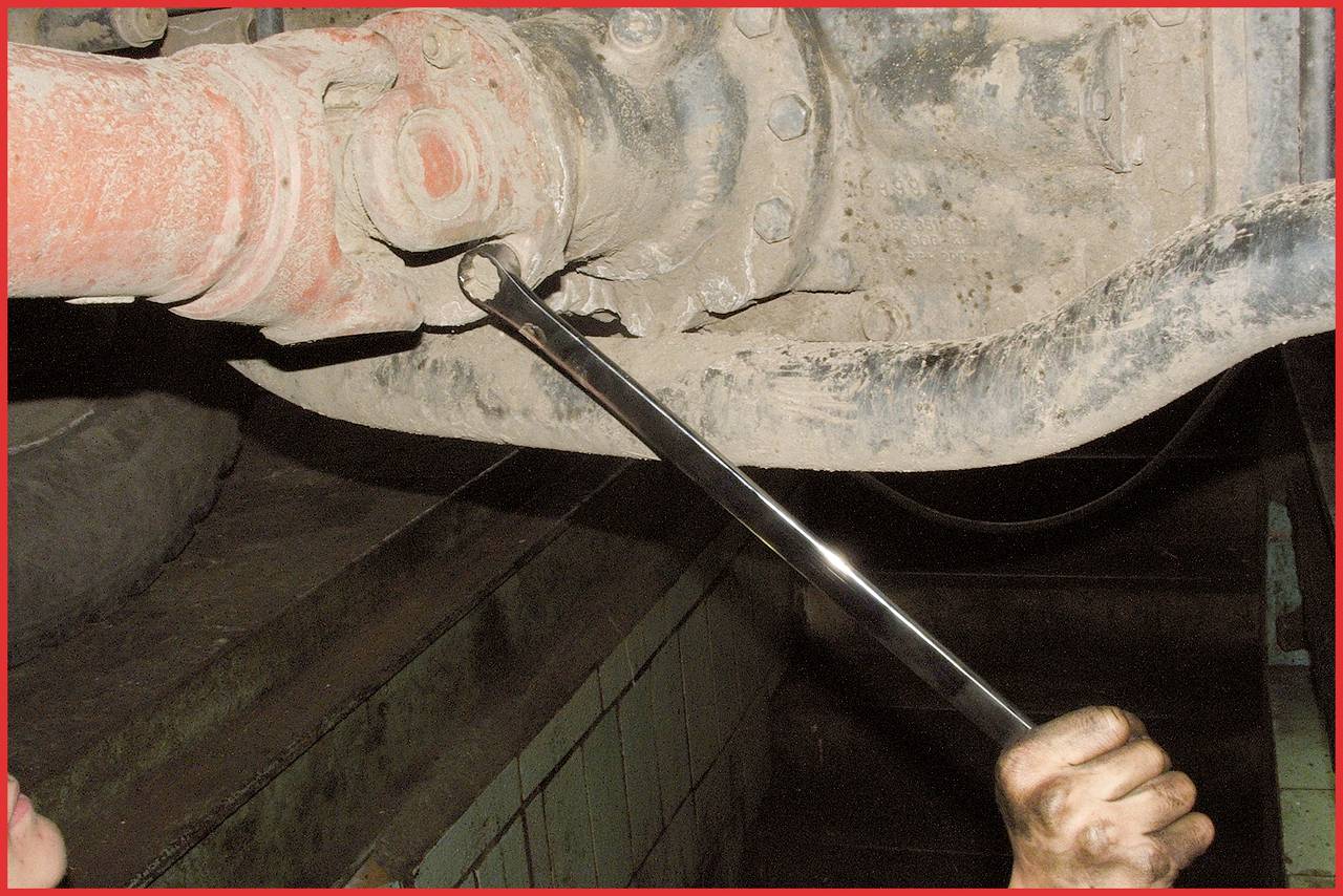 A person is repairing a vehicle undercarriage with a spanner, working on a rusty mechanical connection.