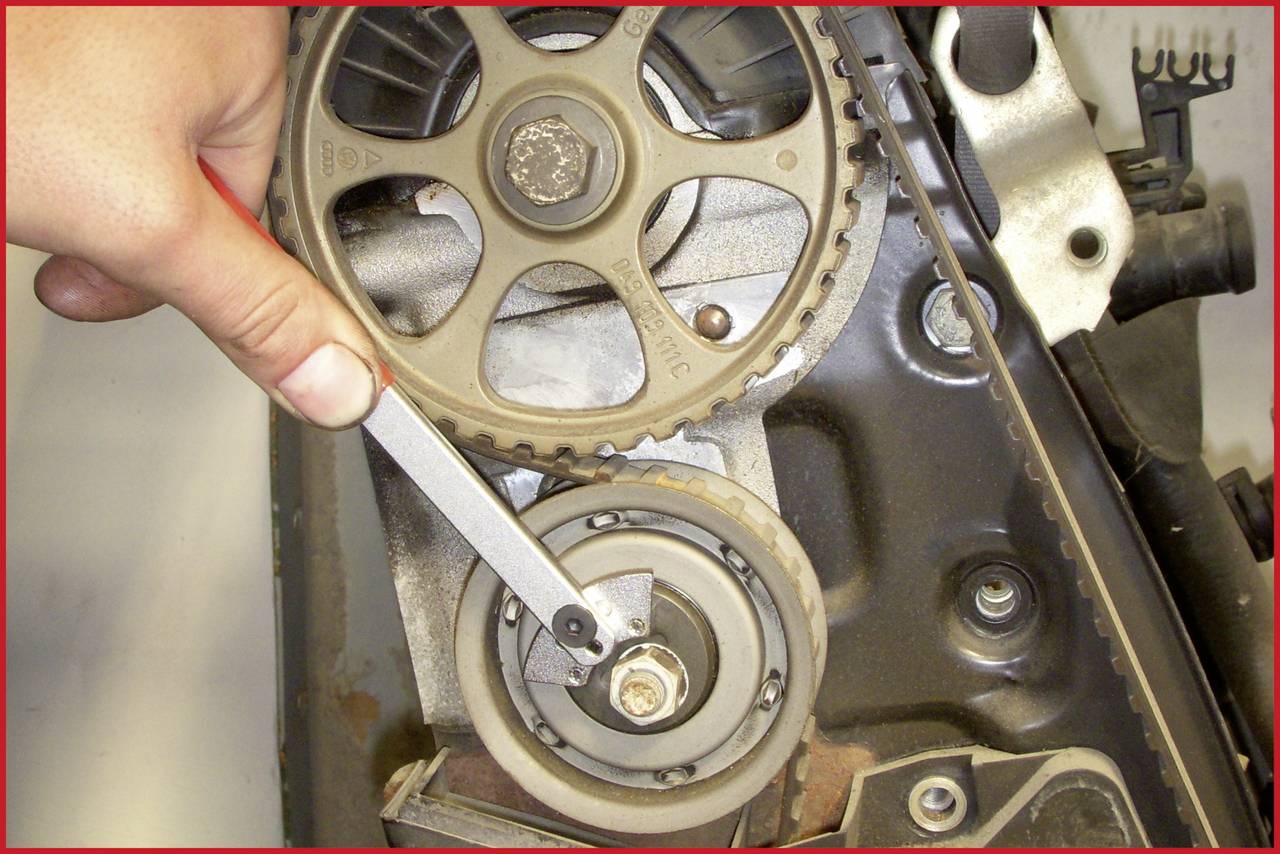 A hand holds a spanner on a timing belt in an engine compartment.