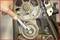 A hand holds a spanner on a timing belt in an engine compartment.