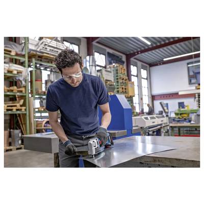 Worker wearing safety glasses and gloves uses an angle grinder on a metal sheet in a workshop<br>