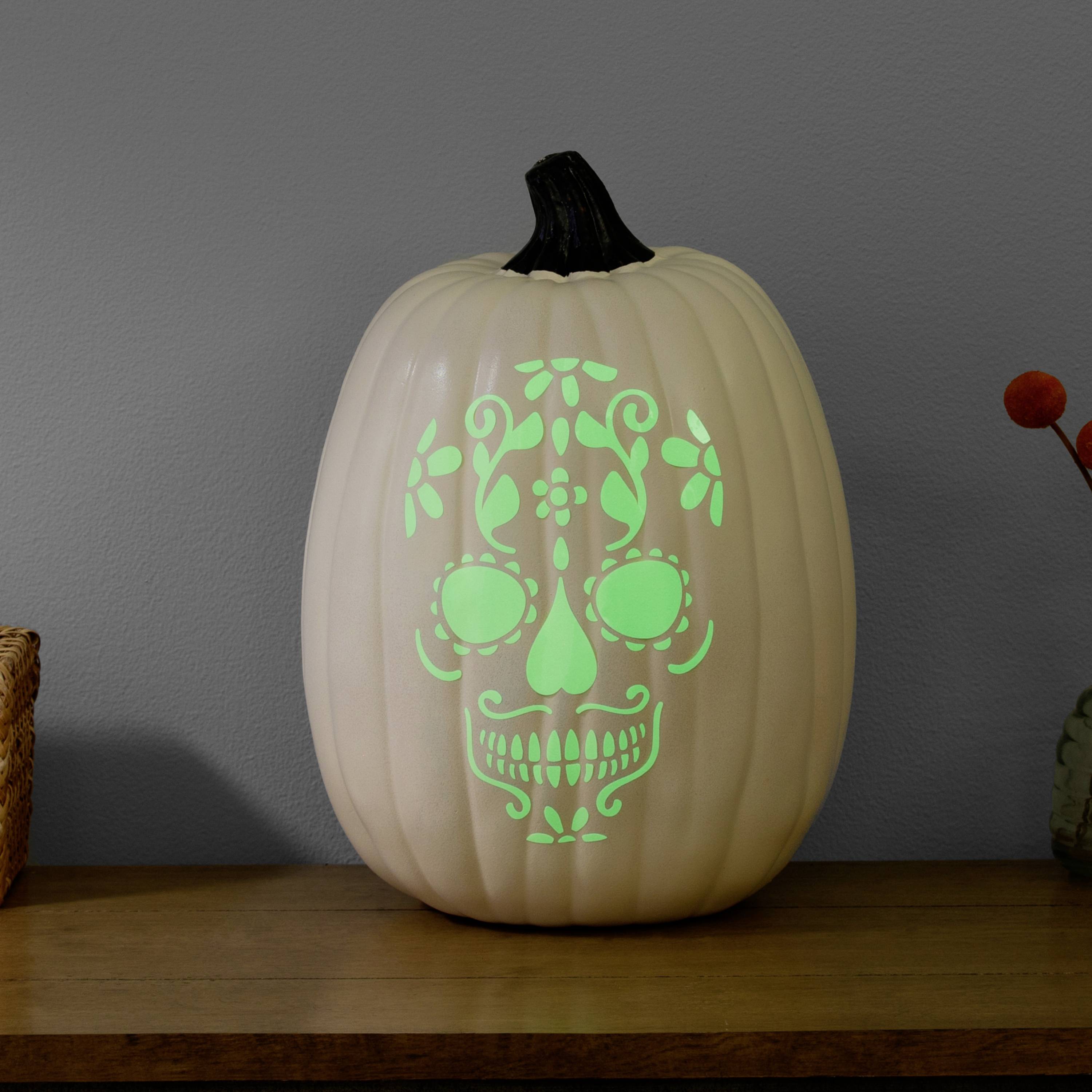 A glowing pumpkin with a carved skull pattern sits on a wooden table.