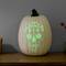A glowing pumpkin with a carved skull pattern sits on a wooden table.
