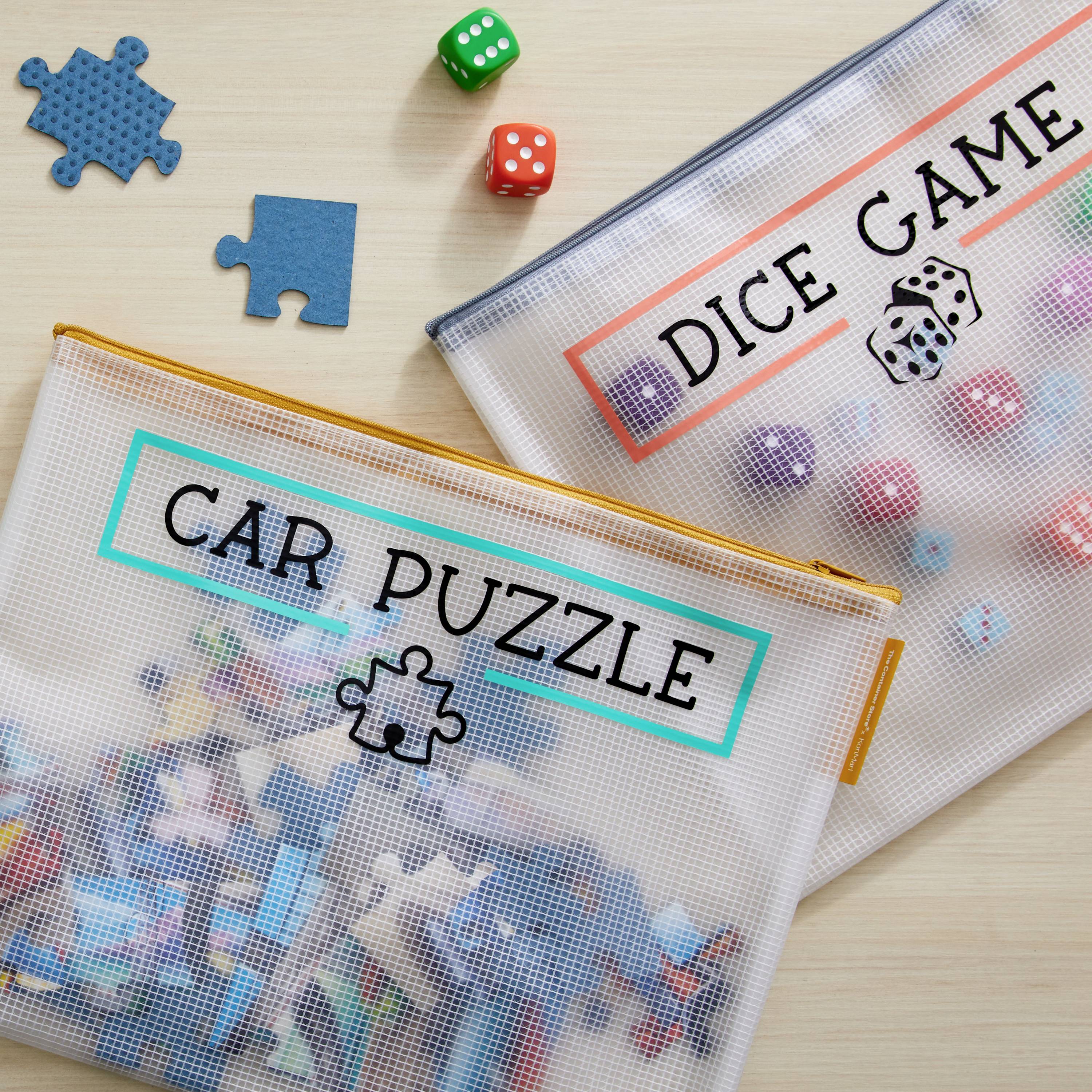 Two transparent bags on a table, one labelled 'CAR PUZZLE', filled with puzzle pieces, the other labelled 'DICE GAME', filled with colourful dice.