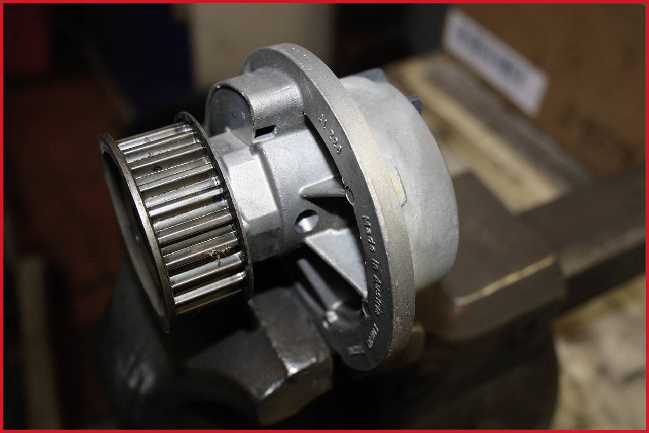 A metal machine part coupling is secured in a vice. It displays gears and is presumably part of an engine.