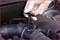 A hand pulls an oil dipstick from a car engine compartment to check the oil level. The engine shows typical signs of dirt and grime.