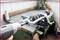 A person is repairing a mechanical part on a workbench with an electric rotary tool and a G-clamp.