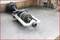 A car part is lying on a workshop floor. It is a drive shaft with visible joints and metal components.