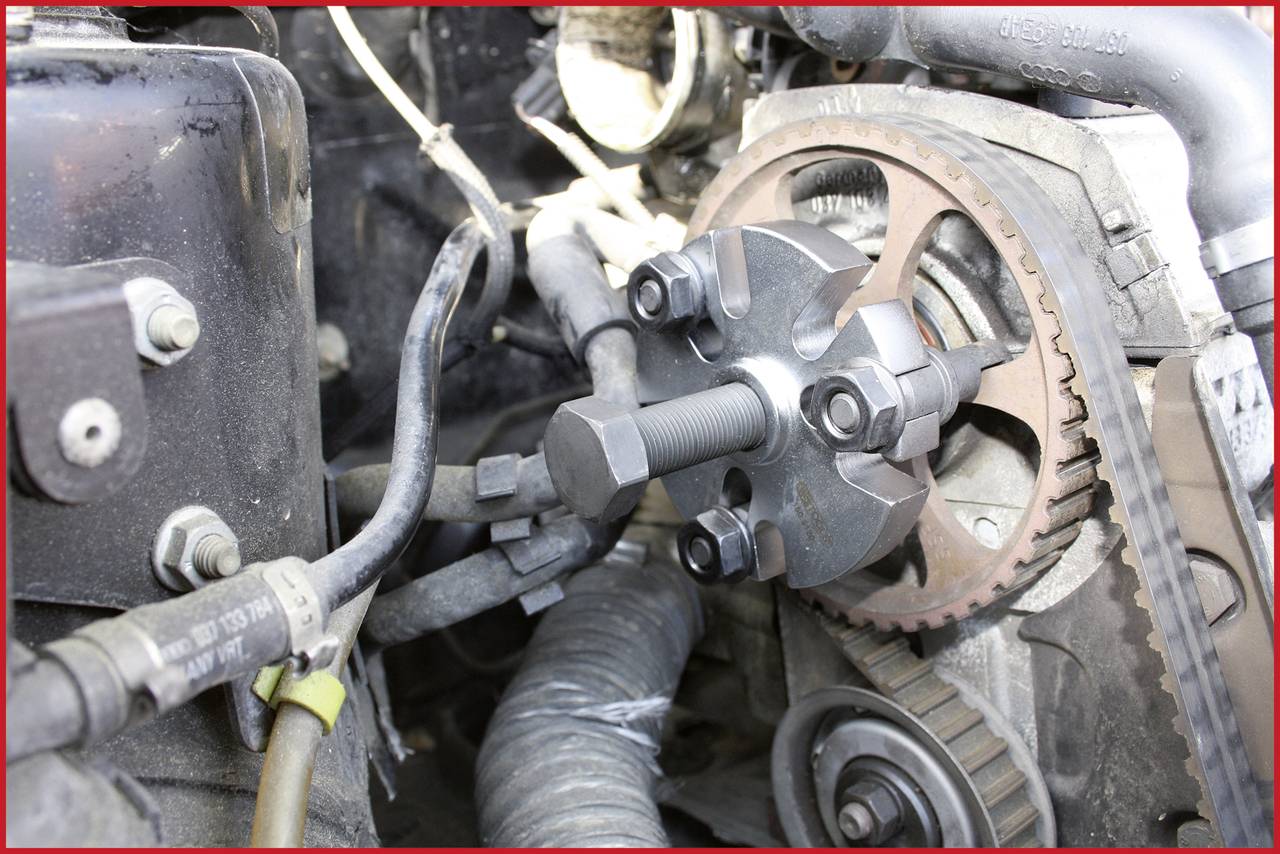 'Close-up of an engine with a timing belt and a specialised tool that secures and adjusts the belt on a toothed wheel.'