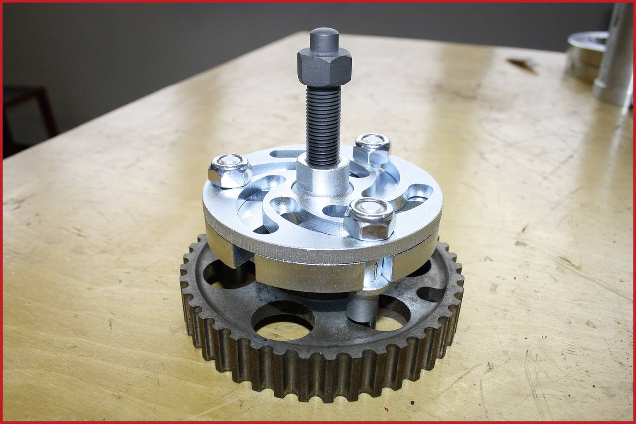 A gear wheel on a wooden table, with a special device with screws above it. Mechanical tool for technical applications.