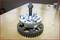 A gear wheel on a wooden table, with a special device with screws above it. Mechanical tool for technical applications.