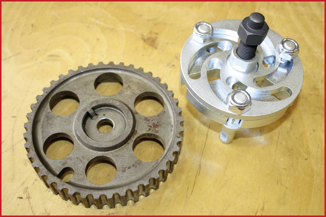 Metal gear wheel next to a silver scraper on a wooden surface. The gear wheel is brown-tinged, the scraper intact and ready for use.