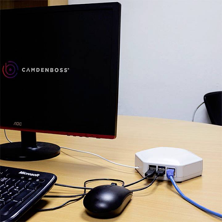 A computer monitor displays a company logo. Next to it, a router with network cables plugged in is visible on a desk.