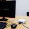 A computer monitor and keyboard are connected to a small white router sitting on a table.