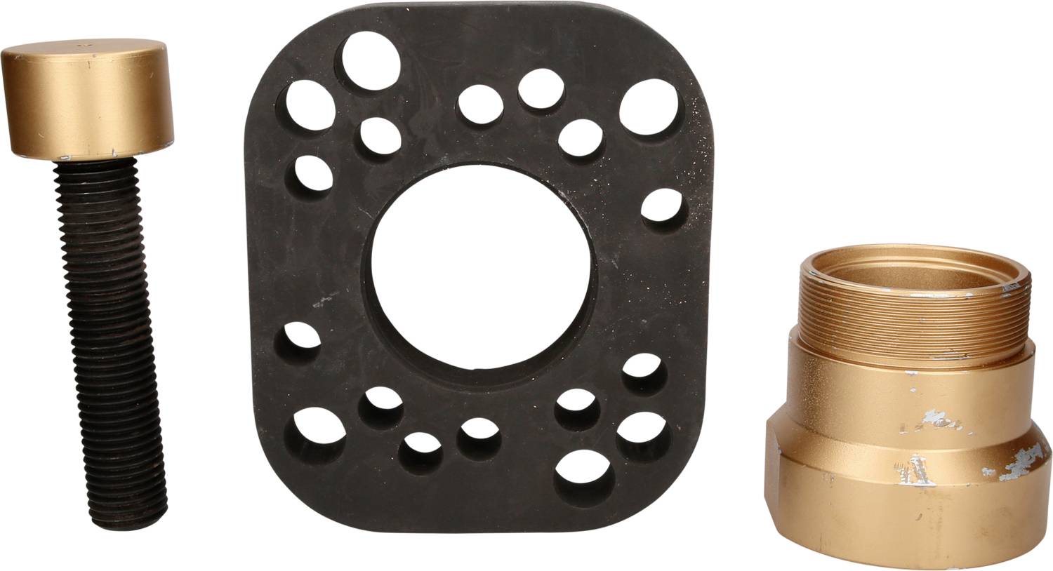 Black adapter plate with numerous holes, gold screw on the left, gold connector on the right. Components of a door lock installation kit.