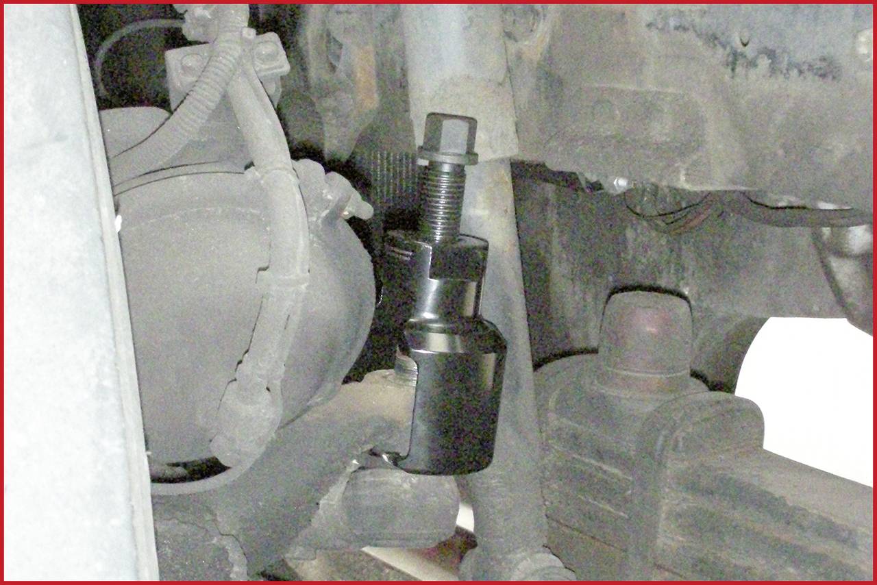 A wheel suspension is being worked on with a puller mounted on a steering knuckle. Mechanical car repair in progress.