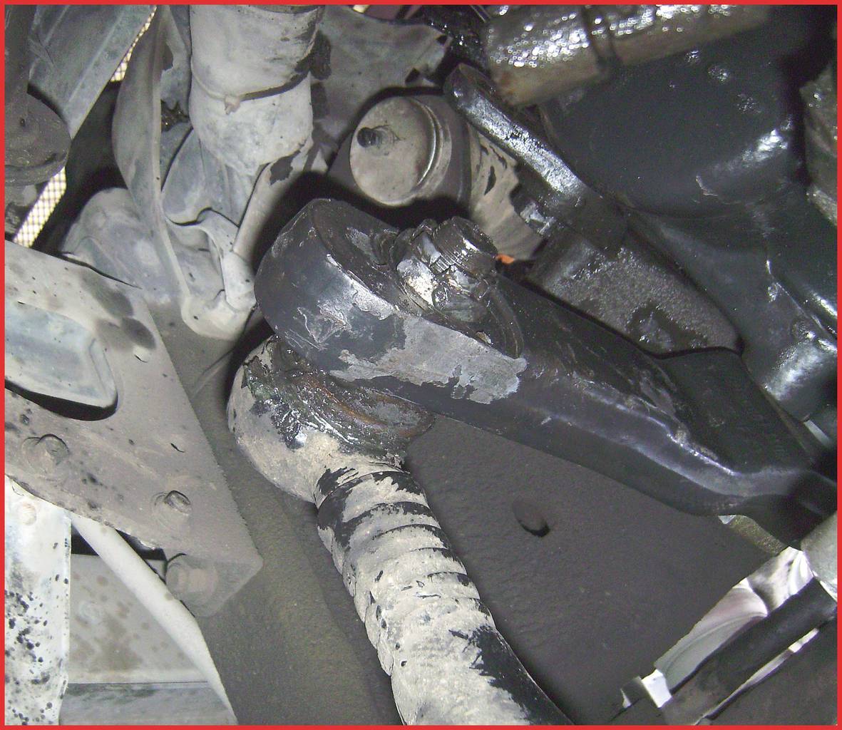 Vehicle suspension system, close-up of metal components and joints, with visible lubricating grease and signs of wear.