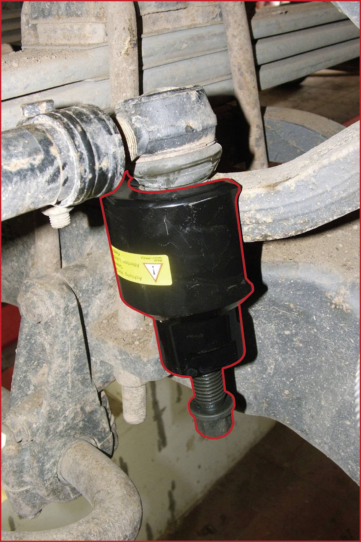 A black tool, marked with a red border, is attached to a dirty metal structure.