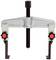 Metal three-arm puller with two red handles and a central screw for removing tightly fitted parts such as gears or bearings.