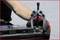 A hand wearing work gloves is using a puller to remove a car battery terminal. The bonnet is open.