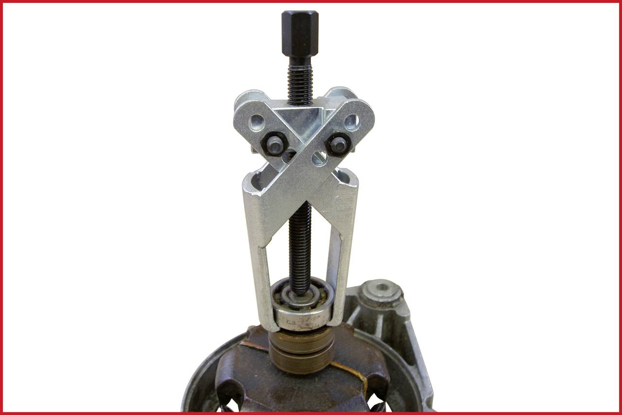 A metal puller is attached to a circular component to remove it. The puller has two arms and a central thread.