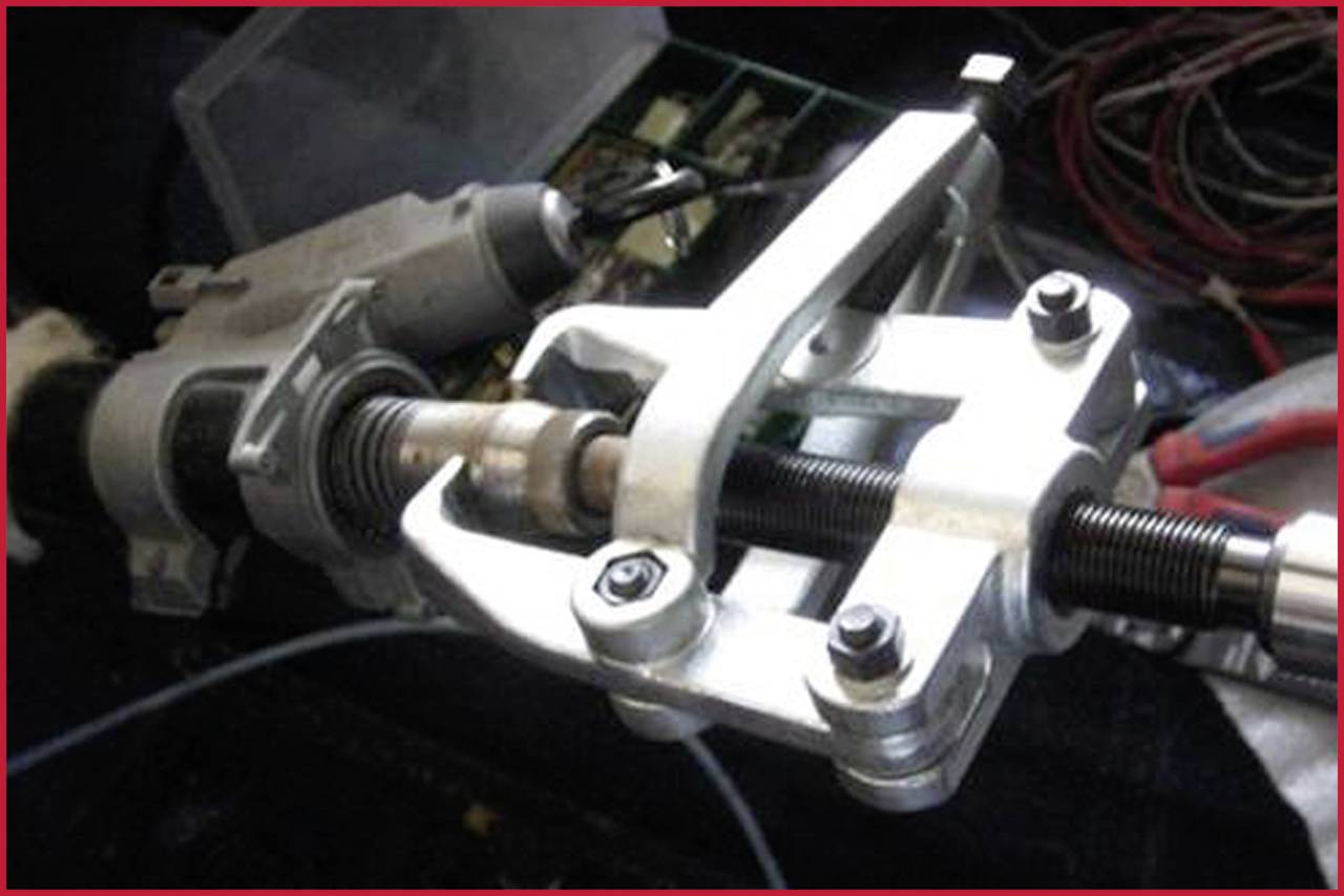 A puller tool grips a metal rod. In the background, electrical tools and cables are lying around.