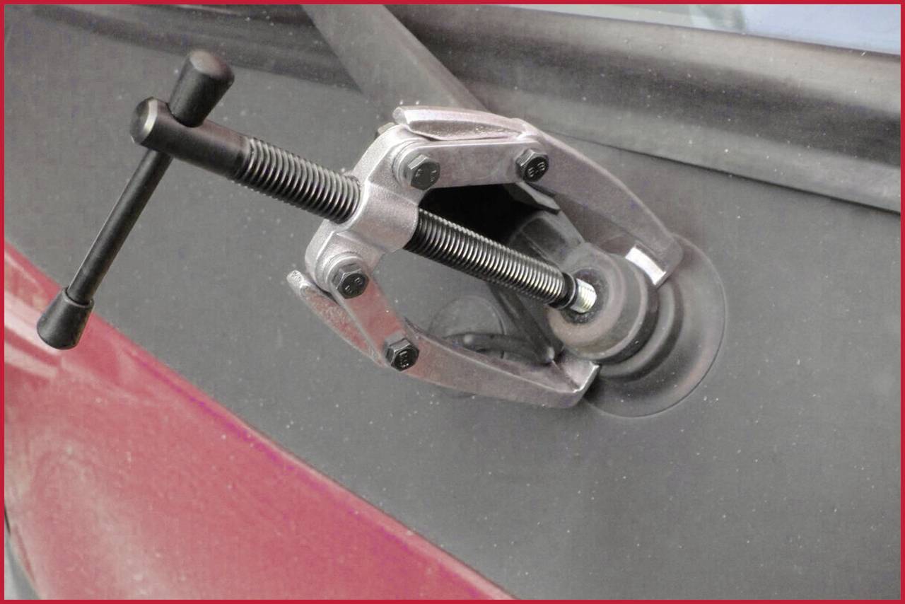 A tool with two gripping arms removes a dent from a red car door.
