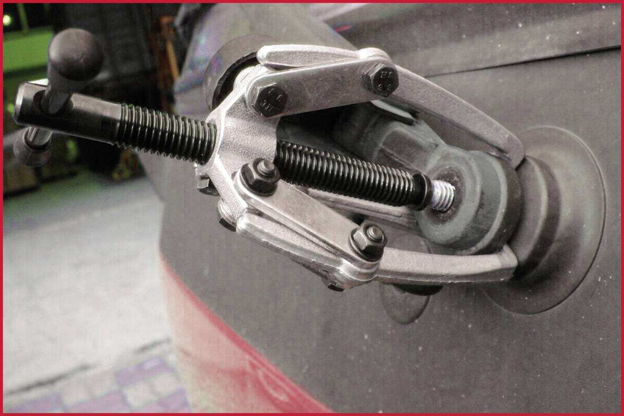 A three-arm puller is attached to a vehicle wheel bearing to remove the bearing. It is aligned with the mounting.