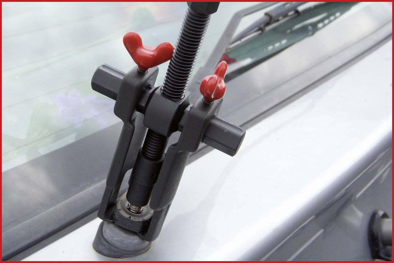 A tool is removing a windscreen wiper arm from a car's windscreen motor. The background shows part of the vehicle.
