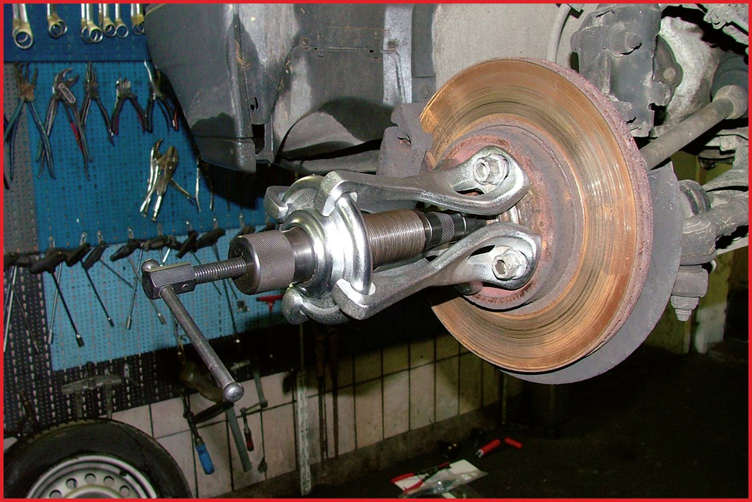 A brake disc puller removes a brake disc from a vehicle. In the background, tools hang on a blue wall.