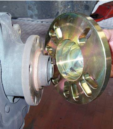 A metal adapter is manually fitted to a vehicle's wheel hub.
