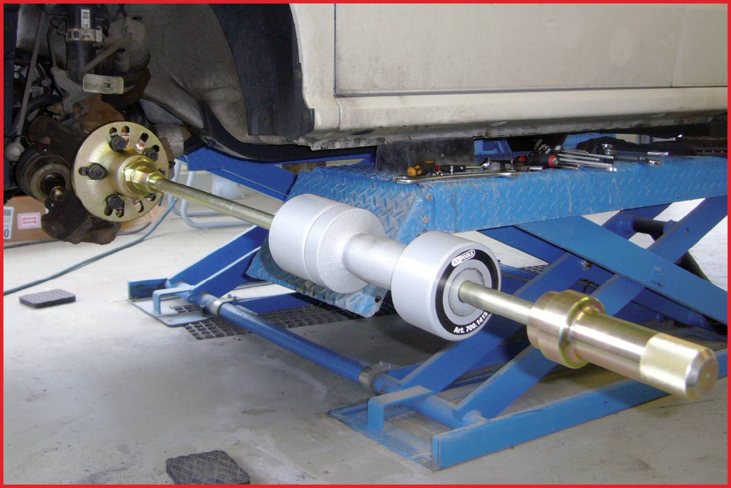 A car is positioned on a vehicle lift, with a mechanic apparently installing some mechanism on the front axle wheel. Working environment.