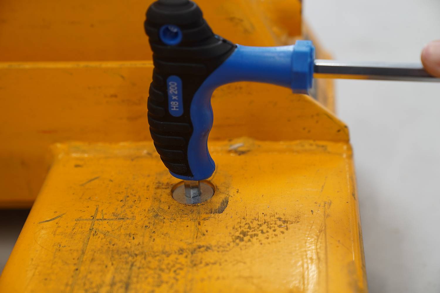A person is using a blue screwdriver to tighten a screw in a yellow metal component.