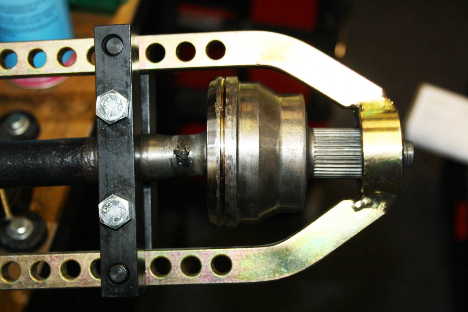 Close-up of an automotive tool removing a wheel bearing or drive shaft, secured with spanners and bolts.