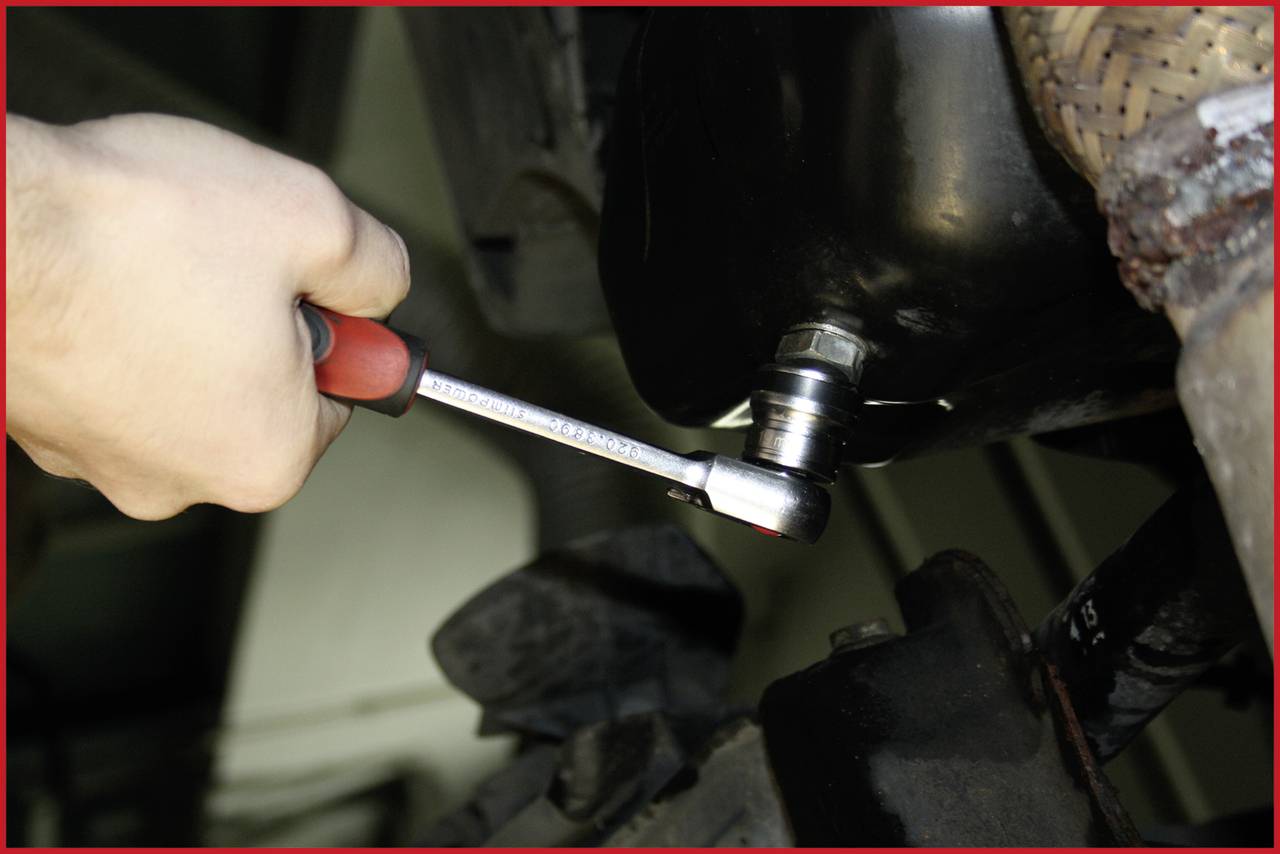 A hand uses a spanner to tighten a screw on a vehicle. Focus is on the spanner and screw.