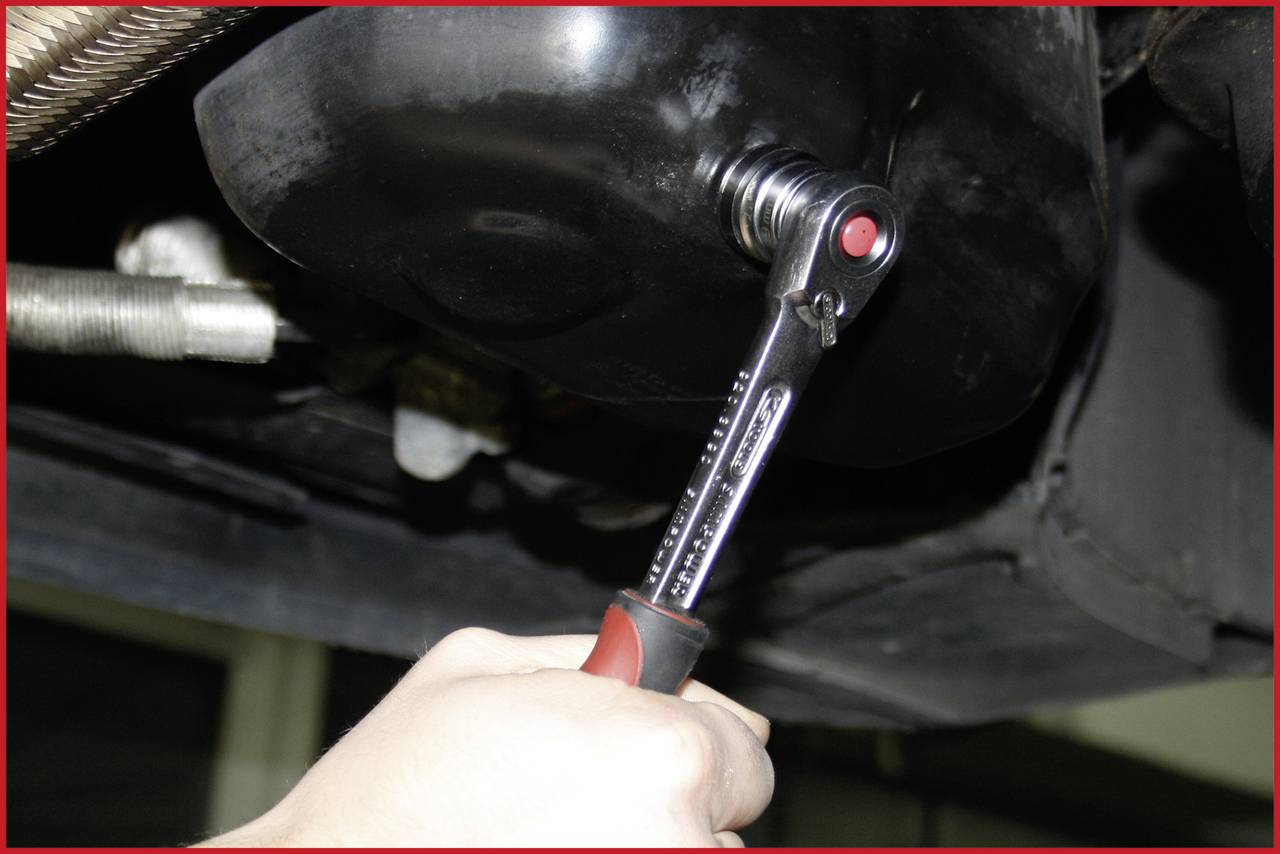 A hand uses a spanner to tighten a screw on a car. It indicates maintenance work being carried out underneath the vehicle.