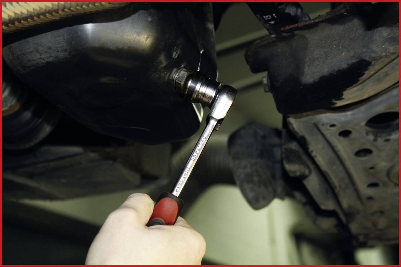 A person is tightening a nut on a vehicle's undercarriage with a spanner, likely during vehicle maintenance.