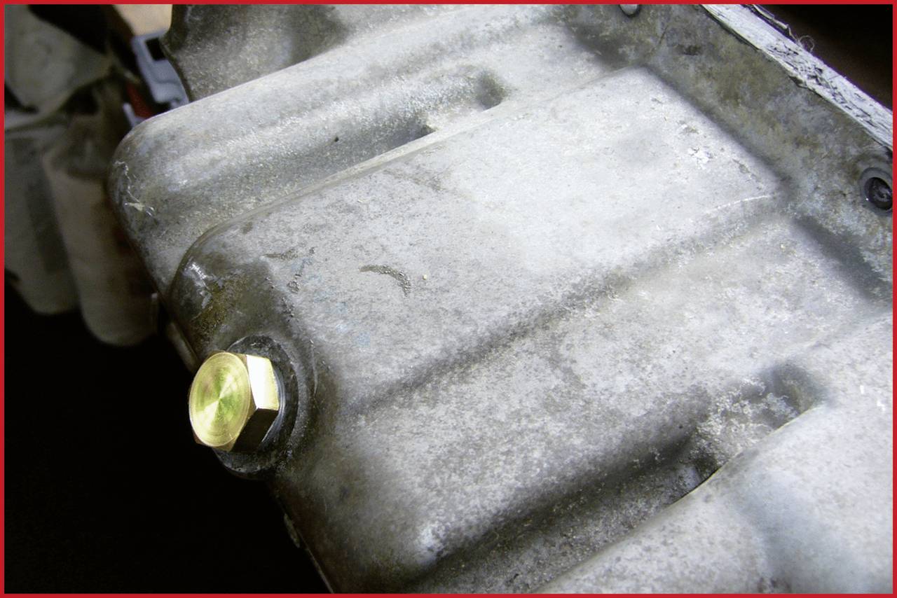 A metal oil sump cap located close by in a vehicle engine compartment.<br><br>Note: The translation maintains the precise technical description using standard British English terminology and phrasing.