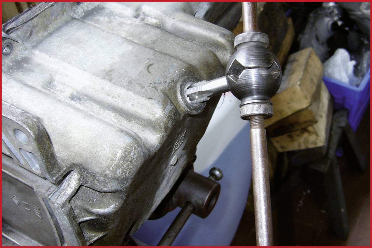 A tap is used to cut a thread into a metal piece. It is attached to a handle and in use.