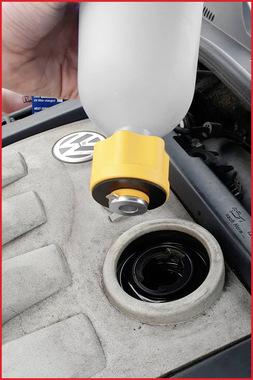 A hand pours oil from a bottle into the engine of a Volkswagen car. Close-up of the engine compartment.