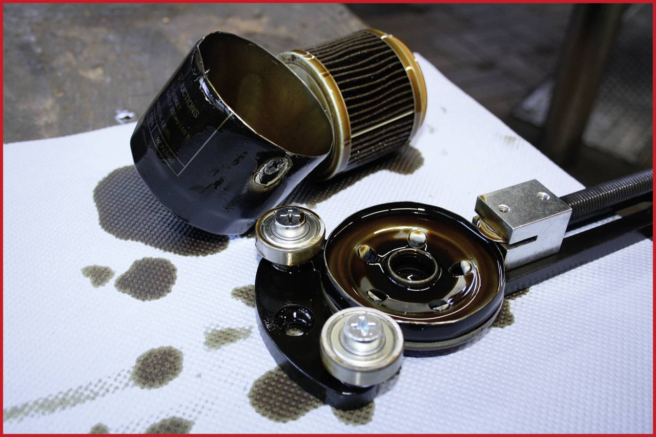 An opened oil filter on a workbench with tools and oil stains. The filter reveals its inner components and oil residue.