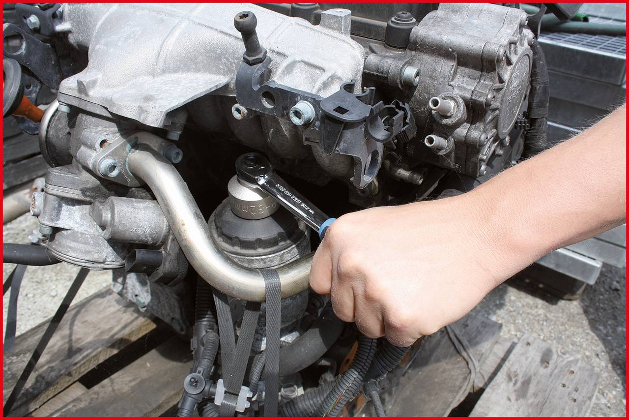A person is tightening a car part, possibly an engine component, with a spanner.<br><br>Note: In British English, "spanner" is typically used instead of "wrench", and the language has been adjusted to sound more naturally British.