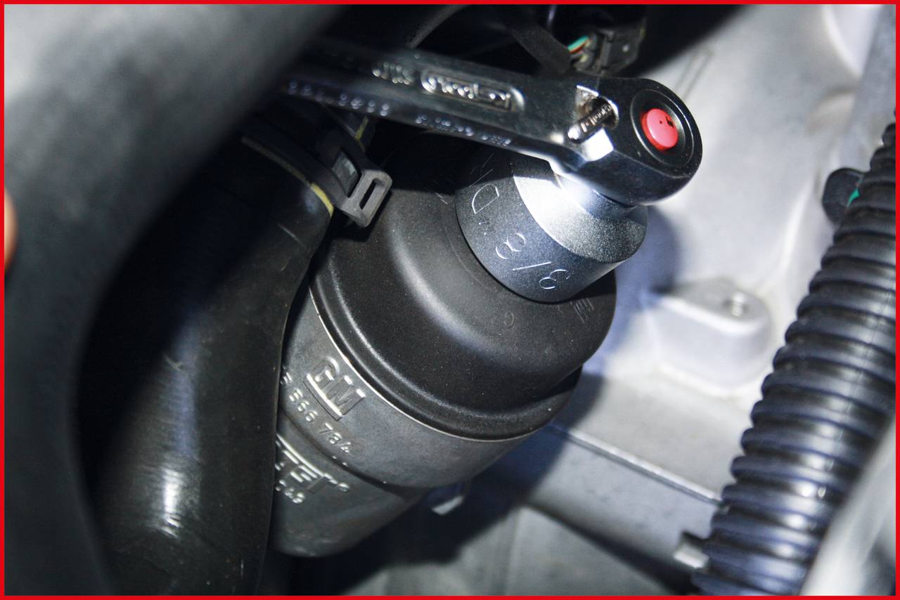 A spanner is used to loosen an oil filter cap in an engine bay.