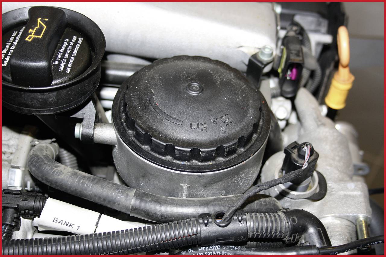 Engine bay with various car components, including the oil filler cap, a black cover, and cables.
