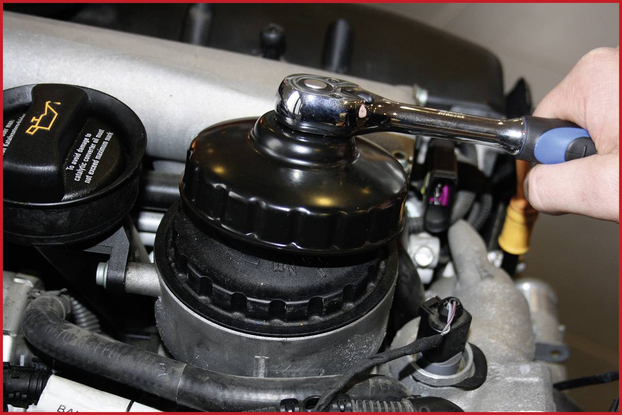 A hand is using a spanner to change an oil filter in a car's engine bay.