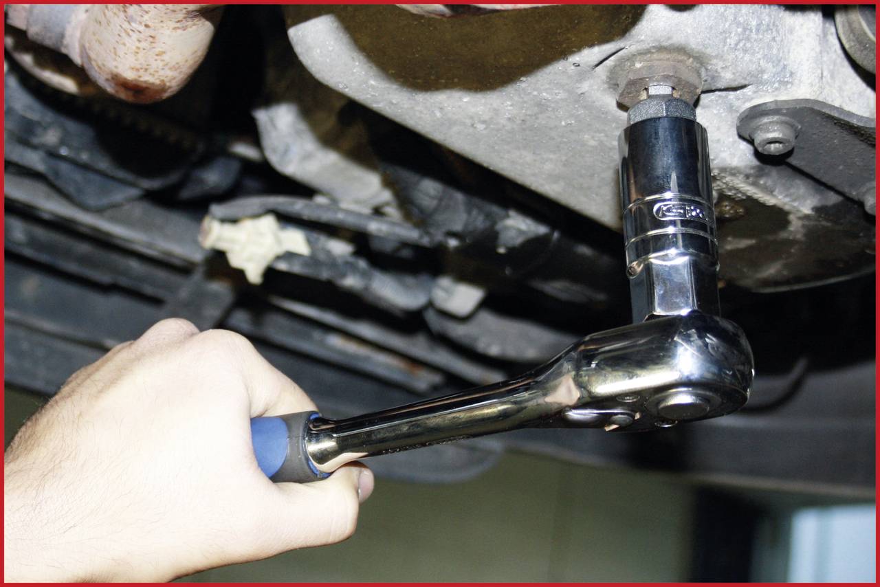 'A hand is tightening a screw with a ratchet on a vehicle motor.'